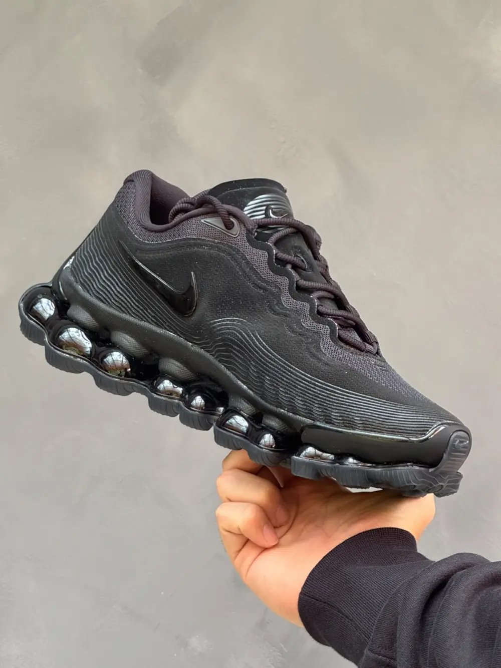 Mano sosteniendo unos tenis de bota negro y naranja